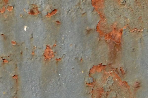 Rusted metal texture with dark orange stains and marks on a surface of chipping light blue paint.